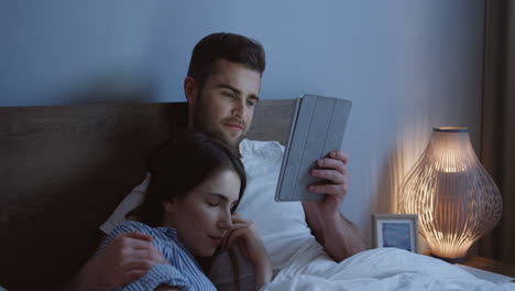 Junges-Kaukasisches-Paar,-Das-Im-Bett-Sitzt-Und-Nachts-Ein-Video-Auf-Dem-Tablet-gerät-Ansieht