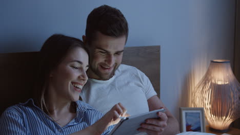Young-caucasian-couple-sitting-the-bed-and-watching-a-video-on-the-tablet-device-at-night