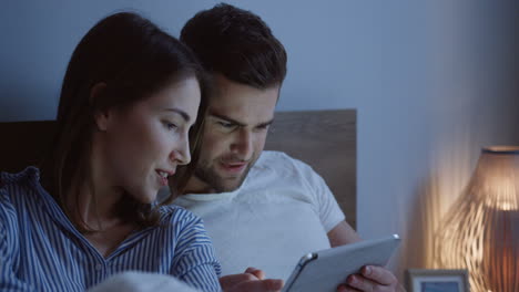 Close-up-view-of-young-caucasian-couple-sitting-the-bed-and-watching-a-video-on-the-tablet-device-at-night