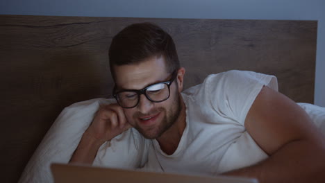 Nahaufnahme-Eines-Lächelnden-Mannes,-Der-Einen-Laptop-Benutzt-Und-Lächelt,-Während-Er-Abends-Etwas-In-Ihrem-Bett-Beobachtet
