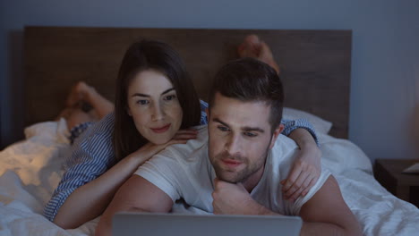 Young-caucasian-couple-lying-in-the-night-on-the-bed-and-watching-a-video-on-the-laptop
