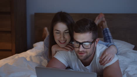 Close-up-view-of-the-young-couple-lying-on-the-bed-in-the-evening-and-watching-something-funny-on-the-laptop