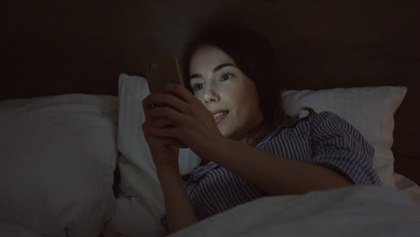 Close-up-view-of-the-charming-Caucasian-woman-with-dark-hair-lying-in-the-bed,-chatting-on-the-smartphone-late-at-night