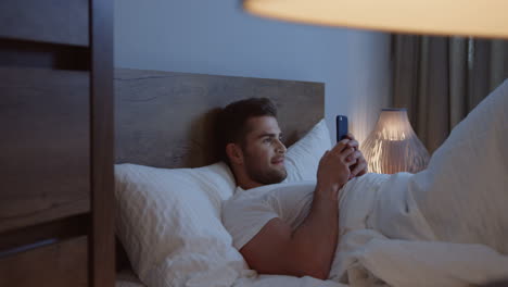 Caucasian-man-lying-in-the-bed,-chatting-on-the-smartphone-late-at-night-before-sleeping