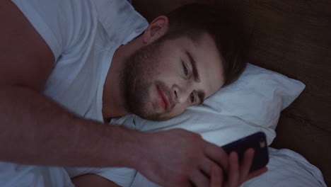 Top-view-of-smiling-Caucasian-man-lying-in-the-bed,-chatting-on-the-smartphone-late-at-night