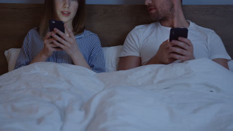 Kaukasisches-Paar,-Das-Smartphones-Benutzt,-Während-Sie-Im-Bett-Unter-Der-Decke-Sitzen