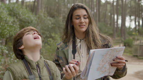 Caucasian-woman-and-her-son-navigating-in-the-forest-with-the-help-of-map-and-compass