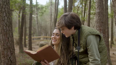 Happy-mother-holding-a-book-and-her-curious-son-reading-it-while-exploring-wildlife-in-a-natural-park
