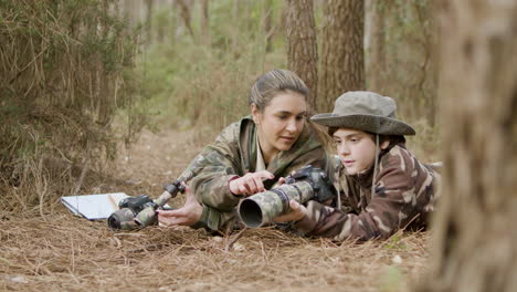 Caucasian-woman-and-her-son-birdwatching-while-lying-on-the-ground-in-the-forest