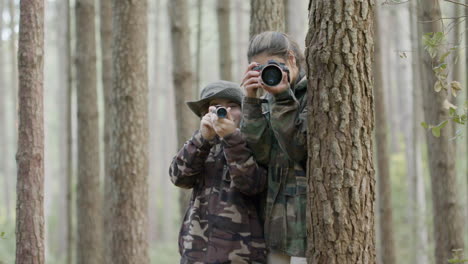 Young-woman-and-boy-standing-between-trees-in-the-forest,-exploring-wildlife-with-monocular-and-camera-and-taking-photos