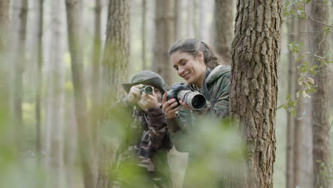 Caucasian-woman-and-boy-standing-between-trees-in-the-forest,-observing-wildlife-with-monocular-and-taking-photos-with-professional-camera
