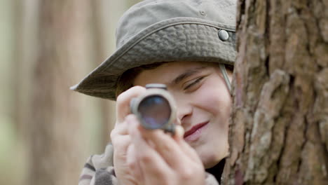 Caucasian-woman-and-boy-standing-between-trees-in-the-forest,-observing-wildlife-with-monocular-and-taking-photos-with-professional-camera