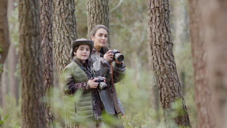 Female-nature-explorer-and-her-son-hiking-in-forest-with-cameras