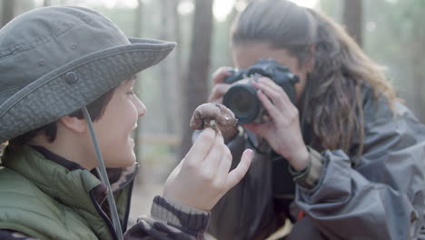 Close-up-of-a-happy-mother-taking-photo-of-her-son-holding-mushroom-in-the-forest
