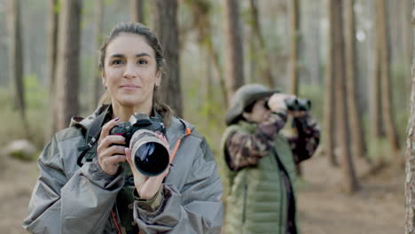 Happy-woman-taking-photos-in-the-forest-and-then-looking-at-the-camera