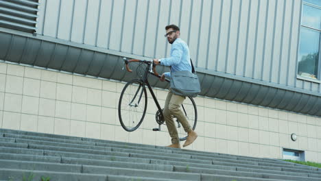 Buen-Mozo-Con-Gafas-Llevando-Su-Bicicleta-Por-Las-Escaleras-Mientras-Va-A-Casa-Del-Trabajo