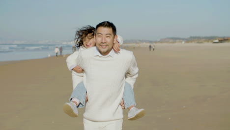 Front-view-of-a-happy-Japanese-dad-giving-his-cute-little-daughter-piggyback-ride