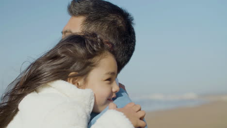 Close-up-shot-of-happy-Japanese-dad-embracing-his-cute-little-daughter-at-the-beach