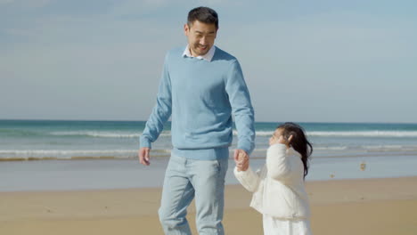 Japanese-father-and-his-cute-little-daughter-walking-along-seashore,-then-man-hugging-his-child