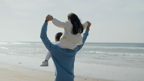 Back-view-of-an-Japanese-father-walking-along-seashore-with-his-daughter-on-his-shoulders-and-having-fun