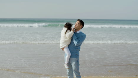 Cariñoso-Padre-Japonés-Sosteniendo-A-Su-Pequeña-Hija-En-Sus-Brazos-En-La-Playa-En-Un-Día-Soleado