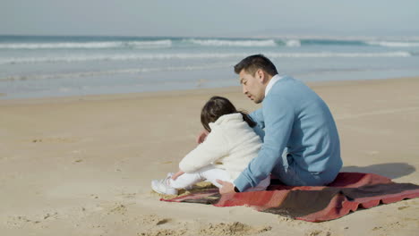 Japanese-dad-and-cute-little-daughter-sitting-on-blanket-at-the-beach