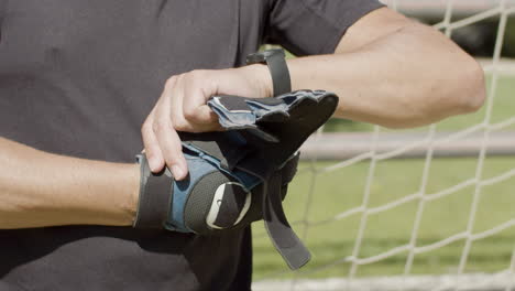 Close-up-of-an-unrecognizable-senior-goalkeeper-wearing-gloves-before-match
