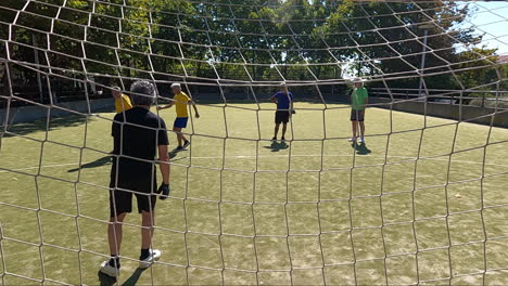 Back-view-of-a-senior-goalkeeper-standing-in-football-goal-training-with-friends-and-catching-ball