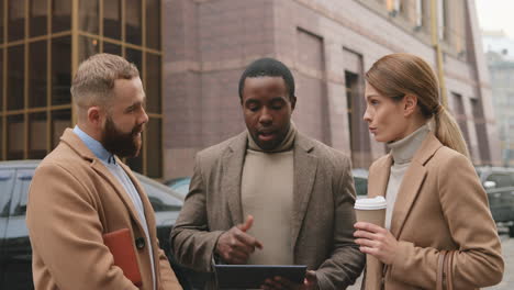Bottom-view-of-caucasian-businesswoman-holding-coffee,-african-american-man-watching-to-a-tablet-and-caucasian-man-talking-in-the-street-in-autumn