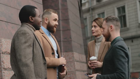 Multiethnic-businessmen-and-Caucasian-businesswoman-holding-a-coffee-standing-together-in-the-street-and-discussing-their-plans-and-new-business-project
