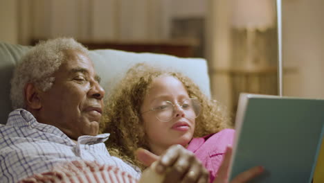 Cute-girl-and-grandpa-lying-on-couch-reading-goodnight-stories
