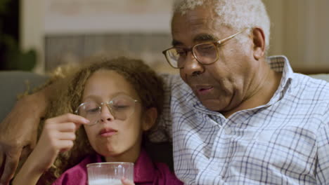 Closeup-of-young-girl-and-granddad-having-late-snack-on-couch