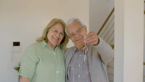 Happy-senior-couple-looking-at-the-camera-and-showing-the-keys-of-their-new-house