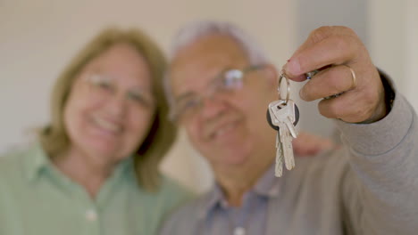 Blurry-senior-couple-smiling-at-the-camera-and-showing-the-keys-of-their-new-house