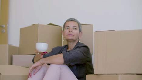 Woman-sitting-on-floor,-drinking-tea-after-moving-to-new-house
