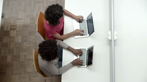 Vista-Superior-De-Mujeres-Escribiendo-En-Computadoras-Portátiles-En-La-Biblioteca