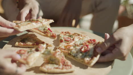 Close-up-shot-of-unrecognizable-people-taking-slices-of-freshly-baked-pizza-from-table
