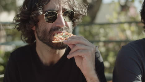 Man-in-sunglasses-eating-pizza-during-rooftop-party-with-friends