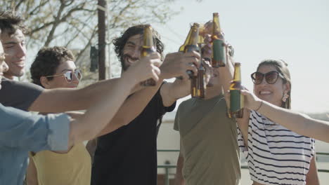Glückliche-Freunde,-Die-Bierflaschen-Anstoßen,-Während-Sie-Eine-Party-Auf-Dem-Dach-Feiern