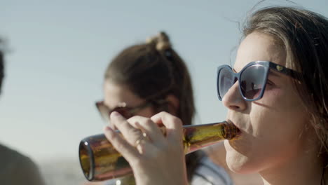 Close-up-of-a-Caucasian-woman-in-sunglasses-drinking-beer-from-bottle-at-party