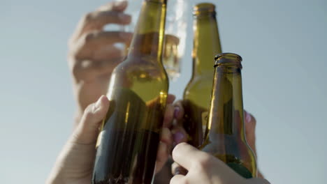 Close-up-of-unrecognizable-friends-raising-and-clinking-bottles-of-beer