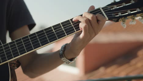 Close-up-of-an-unrecognizable-man-keeping-hand-on-guitar-fretboard-and-playing-music-at-party