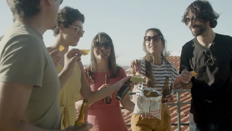 Happy-friends-drinking-beer-and-eating-nachos-at-rooftop-party-on-a-summer-day