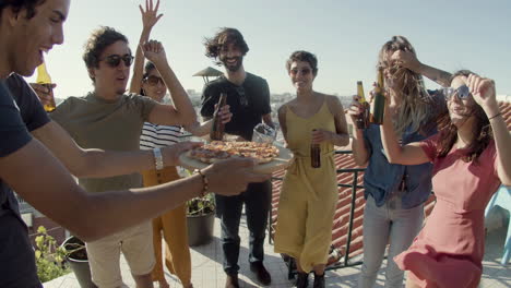 Happy-man-carrying-pizza-to-friends-during-a-rooftop-party