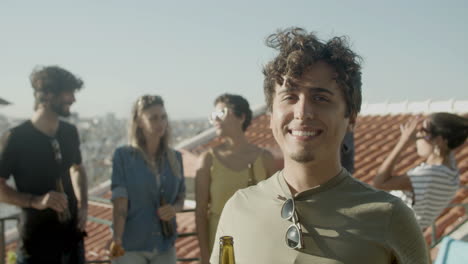 Portrait-of-a-young-Caucasian-man-looking-at-the-camera-and-smiling-while-having-a-rooftop-party-with-friends
