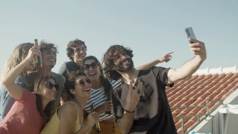 Happy-bearded-man-taking-a-selfie-photo-with-friends-who-holding-beer-bottles-during-a-rooftop-party
