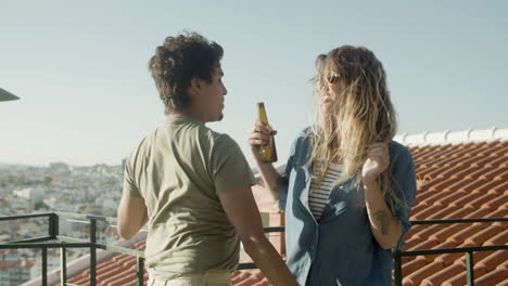 Cheerful-couple-holding-beer-and-dancing-at-rooftop-party