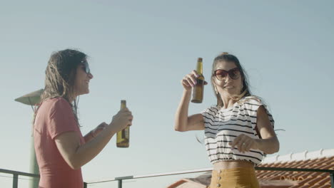 Happy-Caucasian-girls-holding-beers-and-dancing-on-rooftop-during-an-outdoor-party