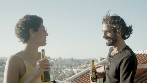 Cheerful-couple-dancing-and-toasting-with-beers-at-rooftop-party