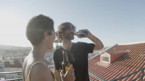 Cheerful-couple-toasting-and-drinking-beer-while-dancing-at-rooftop-party